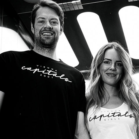 Ein Mann und eine Frau stehen Seite an Seite in einem Aufzug, beide tragen Hemden mit dem Aufdruck "Capitals".